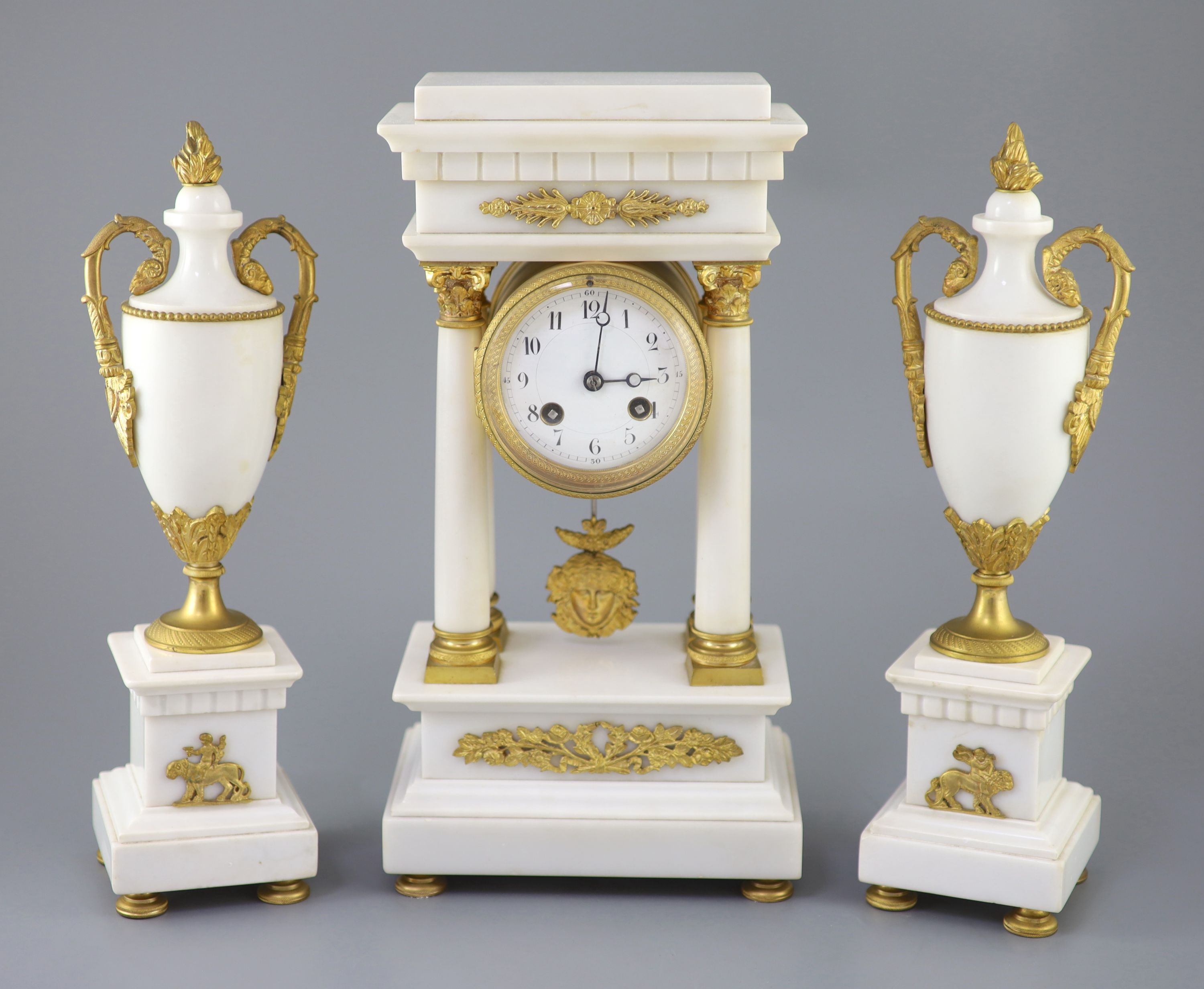 A Louis XVI style ormolu mounted white marble clock garniture, clock 14.5in. urns 13.75in.